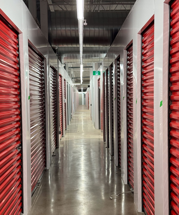 Self-storage hallway with red and grey roll-up doors and illuminated exit sign